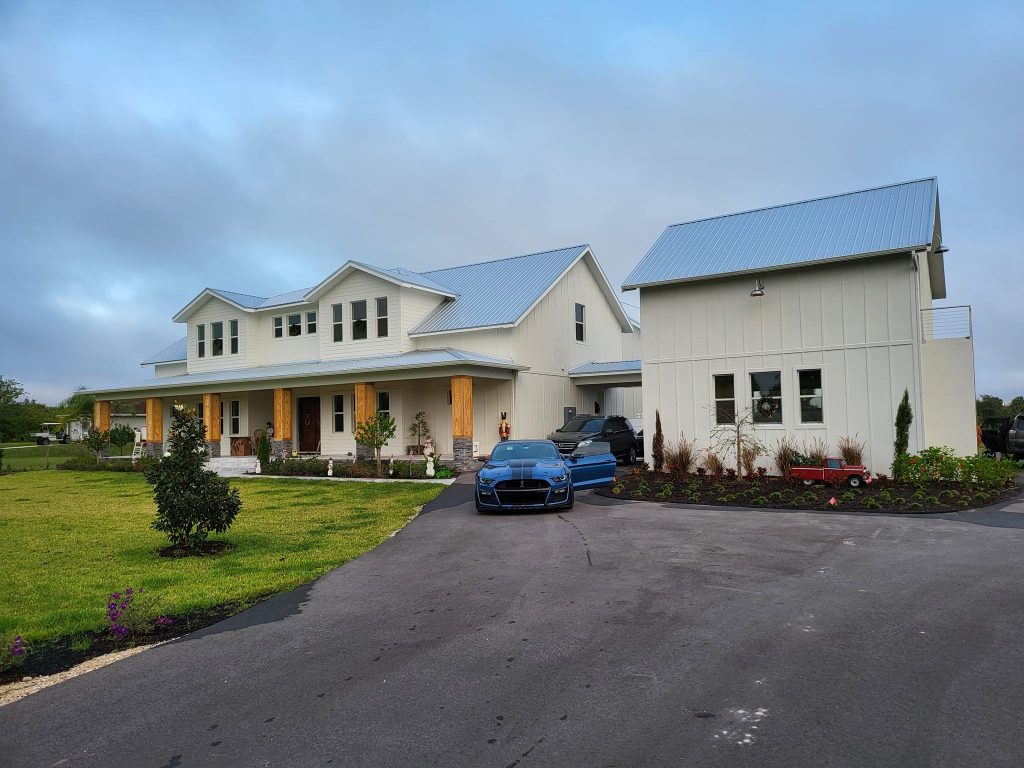 Misty Hollow Naples FL. Modern farmhouse with a metal roof, landscaped yard, and sports car in the driveway