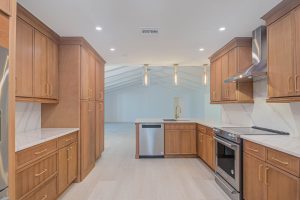 Custom kitchen renovation in Naples, FL featuring natural wood cabinetry, quartz countertops, stainless steel appliances, and modern pendant lighting